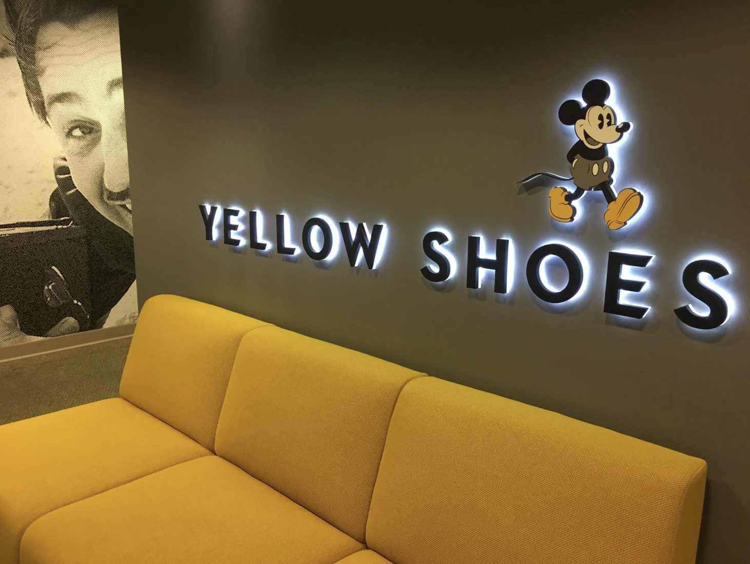 Disney Yellow Shoes studio interior with backlit Mickey Mouse sign and yellow sofa